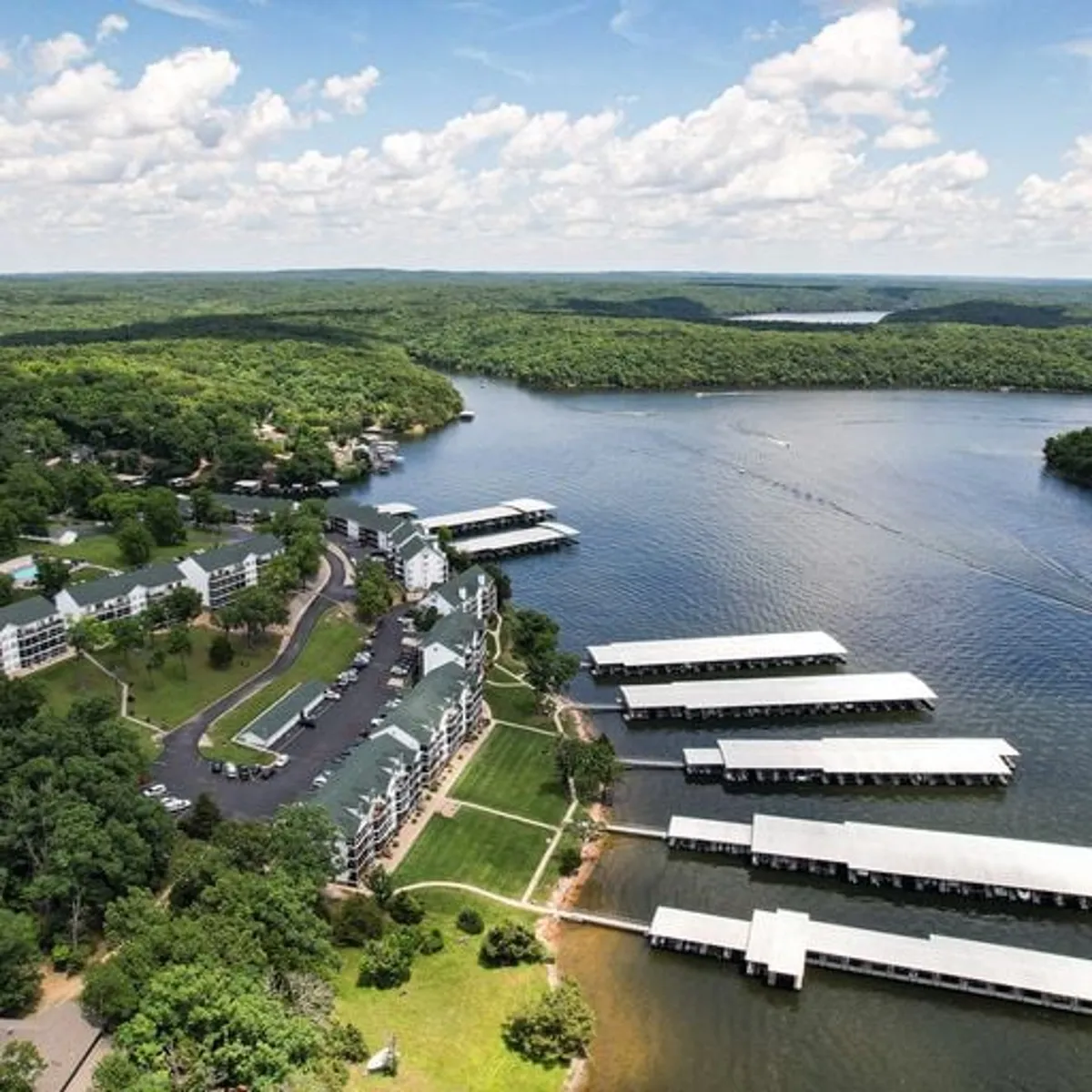 A wide-angle exterior shot featuring the lake, marinas, abundant greenery, and nearby residences. The scene encapsulates the relaxed, inviting mood of lakeside living, with the water beckoning for exploration and enjoyment.