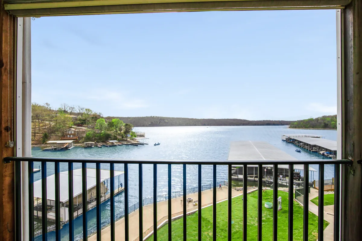 The image showcases a breathtaking, wide-open view of the lake from the condo's lawn, with a private dock extending over the water. Lush green grass leads to the shoreline, framed by a serene blue sky. The scene invites activities like relaxing outdoors, enjoying morning coffee, or hosting a sunset barbecue overlooking the water.