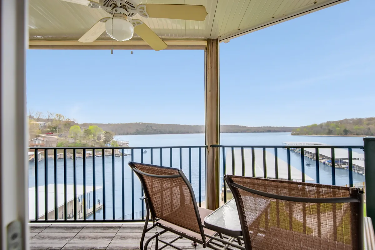 A covered outdoor deck with comfortable seating overlooking the tranquil lake. The space includes a ceiling fan and is styled for both relaxation and socializing, with clear views of boats and the surrounding nature.