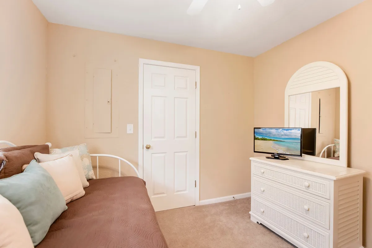 A cozy third bedroom with a daybed, decorative pillows, dresser, mirror, and television creates a multifunctional retreat. The room feels inviting and practical for either relaxation or additional sleeping needs.