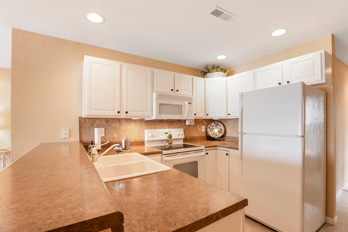 A bright, modern kitchen with white cabinets, ample countertop space, and kitchen appliances. Decorative touches like a stylish plate add a homey feel, while the setup is clean and thoughtfully arranged.