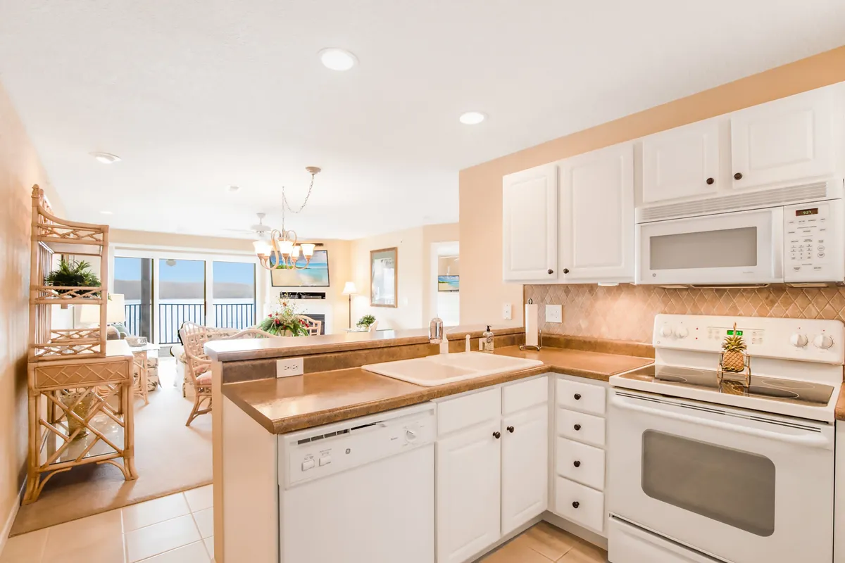 A spacious, modern kitchen with a prominent island, sleek kitchen cabinets, built-in appliances including a microwave and dishwasher, and an open dining area with large windows letting in ample natural light. The scene suggests an inviting space for cooking and gathering, with views that connect to the outdoors.