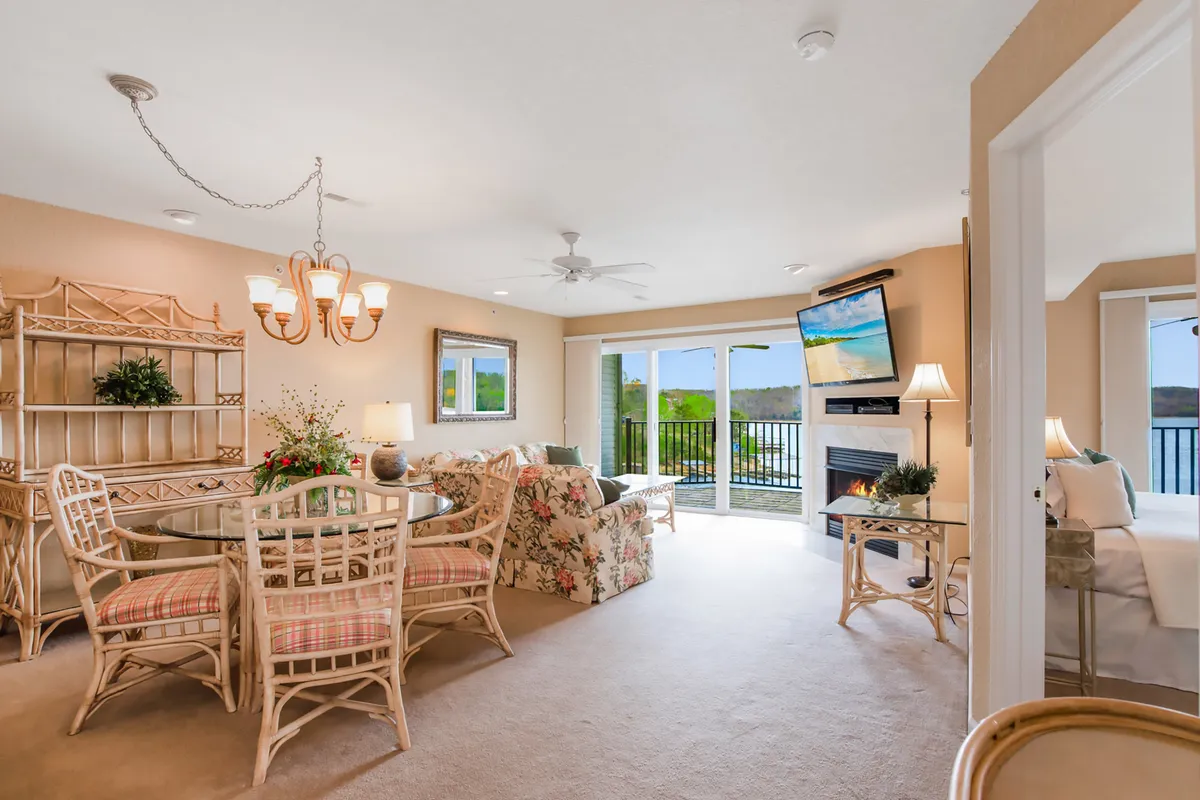 A spacious, light-filled living and dining area with a cozy sofa, a large dining table, and expansive windows framing lake views. The room feels welcoming and perfectly suited for relaxation or social gatherings, with natural light pouring in and a fireplace adding warmth.