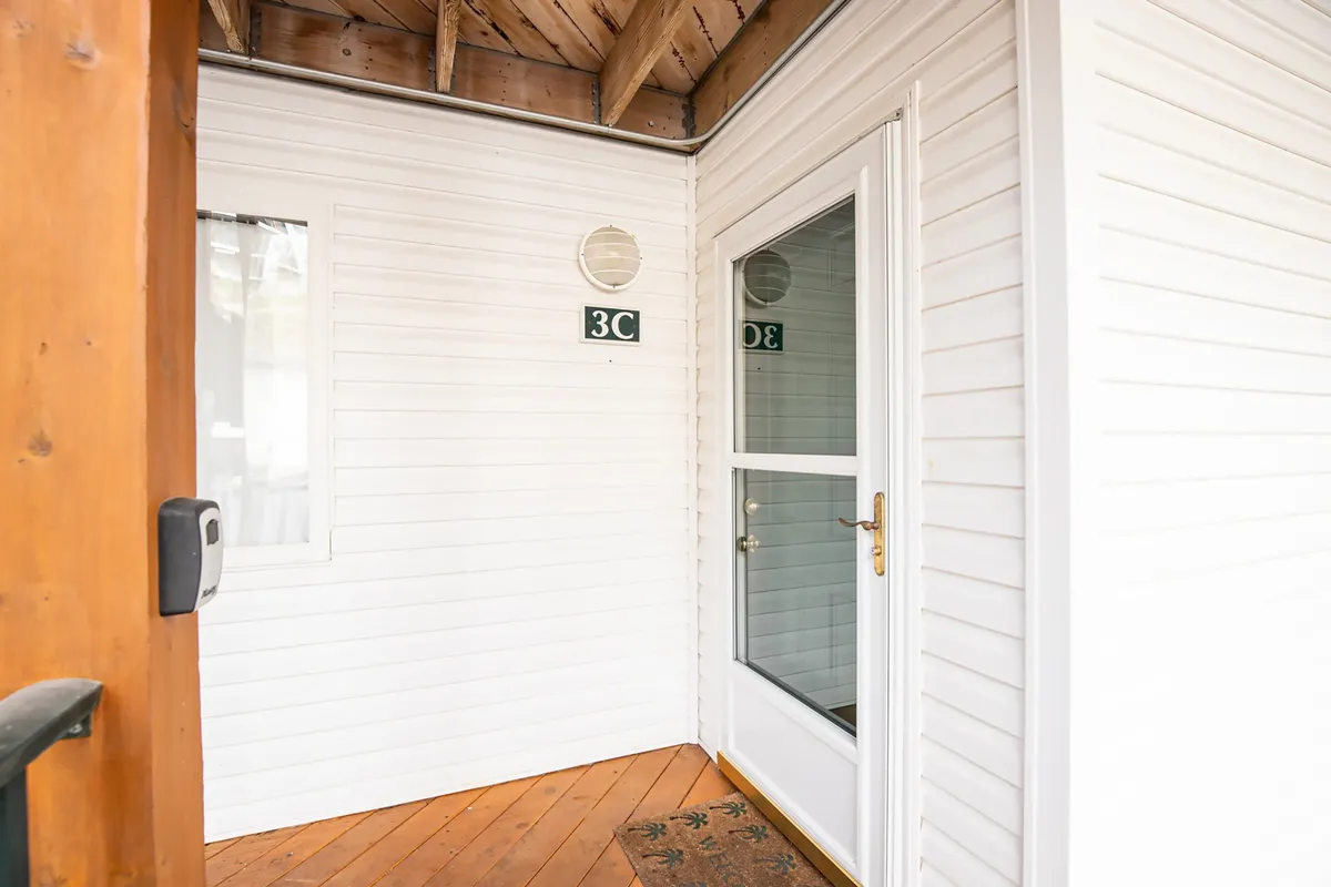 This image showcases the entrance door of the condo, featuring inviting wooden flooring and a visible house number. The area appears tidy and welcoming, setting a secure and well-maintained first impression for guests.