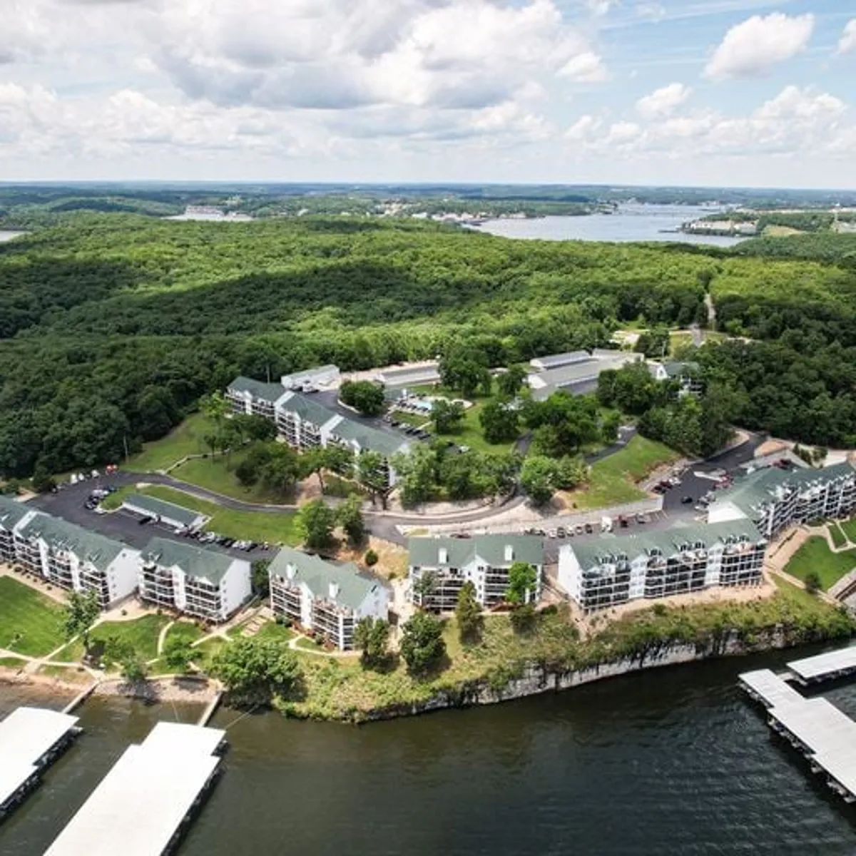 An inviting view of waterfront properties and marina docks nestled among lush greenery. The serene setting includes walkways, roadways, and the lake itself, suggesting easy access to both water and land-based exploration.
