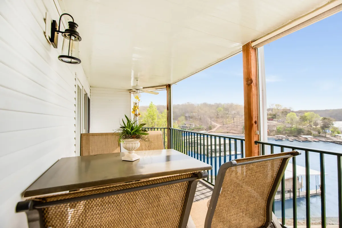 A tranquil deck scene with a table and chairs arranged for relaxation, a potted plant adding a touch of greenery, and a serene view of the water stretching out beyond the railing. The setting is intimate and encourages leisure, whether for reading, sipping coffee, or socializing with friends while enjoying lakefront views.